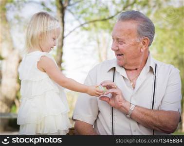 Cute Baby Girl Handing Easter Egg to Grandfather Outside at the Park.