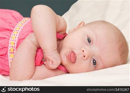 Cute baby girl toddler on bed looking at camera showing her tongue