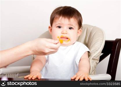 Cute baby infant boy girl expresses dislike disgust for food fed by spoon.