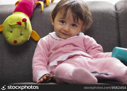 Cute baby leaning on sofa with water bottle and looking away