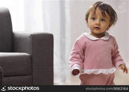 Cute baby looking away while standing in living room at home