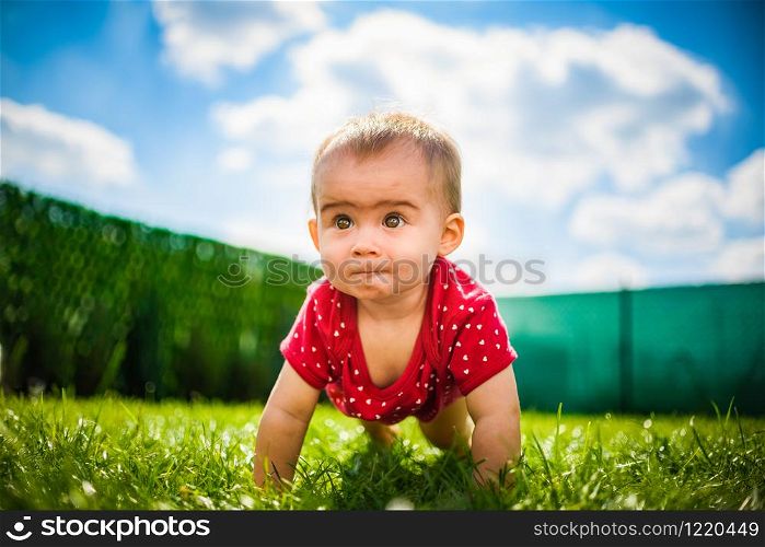 Cute baby on all fours in red body on green grass with blue sky and clouds