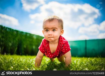 Cute baby on all fours in red body on green grass with blue sky and clouds