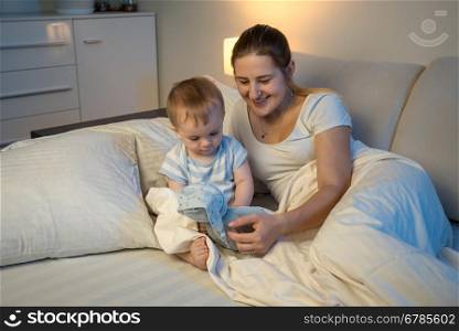 Cute baby playing with doll on bed with mother