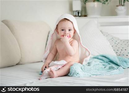 Cute baby sitting on bed covered in towels