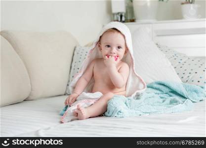 Cute baby sitting on bed covered in towels and playing with toy