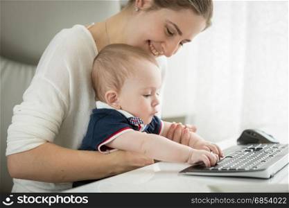 Cute baby sitting on mothers lap and typing on keyboard
