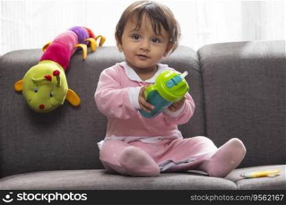 Cute baby sitting on sofa with water bottle and looking away