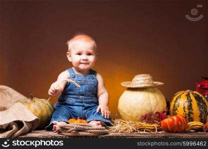 Cute baby with ears of wheat in the hands posing on the background of pumpkins.. Postcard to the day of Thanksgiving