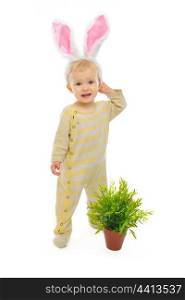 Cute baby with rabbit ears standing near pot with a plant isolated on white