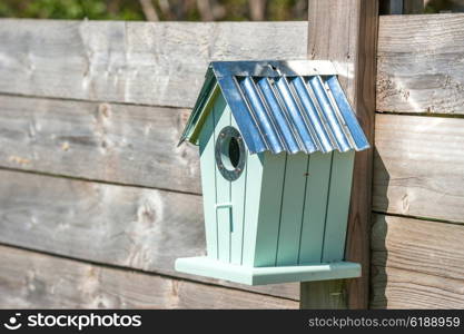 Cute birdhouse hanging on a wooden fence in a garden