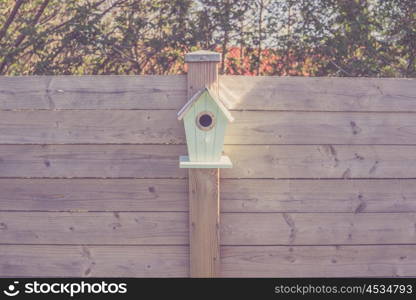 Cute birdhouse on a wooden fence in a garden