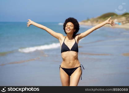 Cute black girl opening her arms on the beach to enjoy her holiday in the sun.. Cute black woman opening her arms on the beach to enjoy her holiday in the sun.