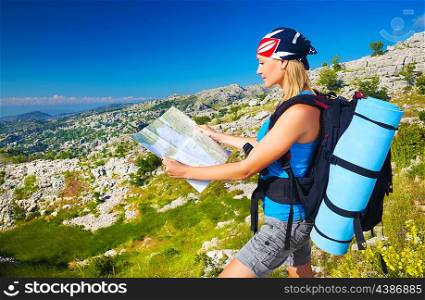 Cute blond girl in the mountains looking way on the map, summer vacation, active lifestyle, tourism and expedition concept