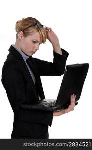cute blonde businesswoman with laptop frowning with glasses raised