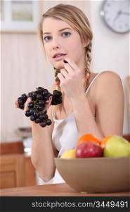 cute blonde eating red grapes in kitchen