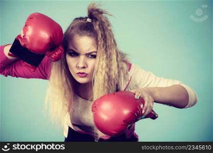 Cute blonde girl female boxer with big fun red gloves playing sports boxing studio shot on blue. Cute girl in red gloves playing sports boxing