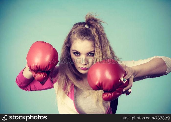 Cute blonde girl female boxer with big fun red gloves playing sports boxing studio shot on blue. Cute girl in red gloves playing sports boxing