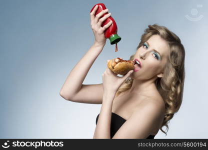 cute blonde lady with fashion style eating hot-dog and putting tomato ketchup on. Glutton woman.