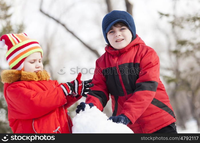 Cute boy and girl building snowman in winter park. Winter active games