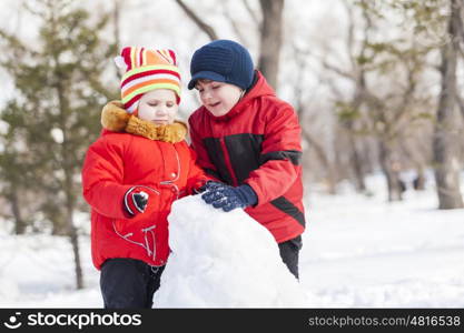 Cute boy and girl building snowman in winter park. Winter active games