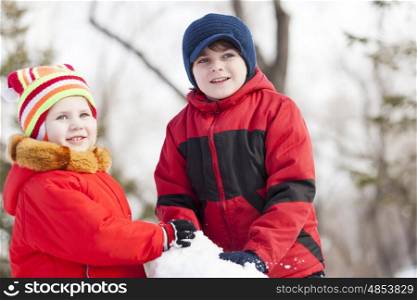 Cute boy and girl building snowman in winter park. Winter active games
