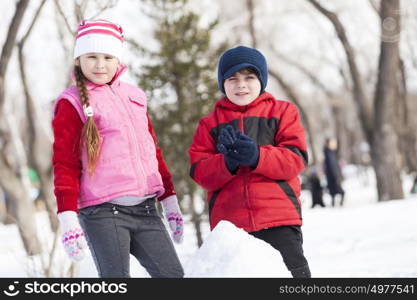 Cute boy and girl building snowman in winter park. Winter active games