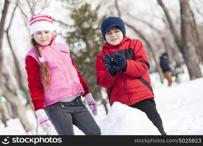 Cute boy and girl building snowman in winter park. Winter active games