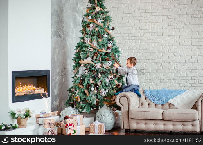 Cute boy decorates the Christmas tree with Christmas balls, gifts under the Christmas tree. Merry Christmas.. Cute boy decorates the Christmas tree with Christmas balls, gifts under the Christmas tree.