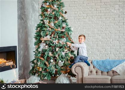 Cute boy decorates the Christmas tree with Christmas balls, gifts under the Christmas tree. Merry Christmas.. Cute boy decorates the Christmas tree with Christmas balls, gifts under the Christmas tree.