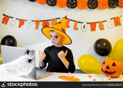 Cute boy in costume sitting behind a table in Halloween theme decorated room. Halloween with safety measures from Covid-19. Halloween holiday concept.. Cute boy in costume sitting behind a table in Halloween theme decorated room. Halloween holiday concept.