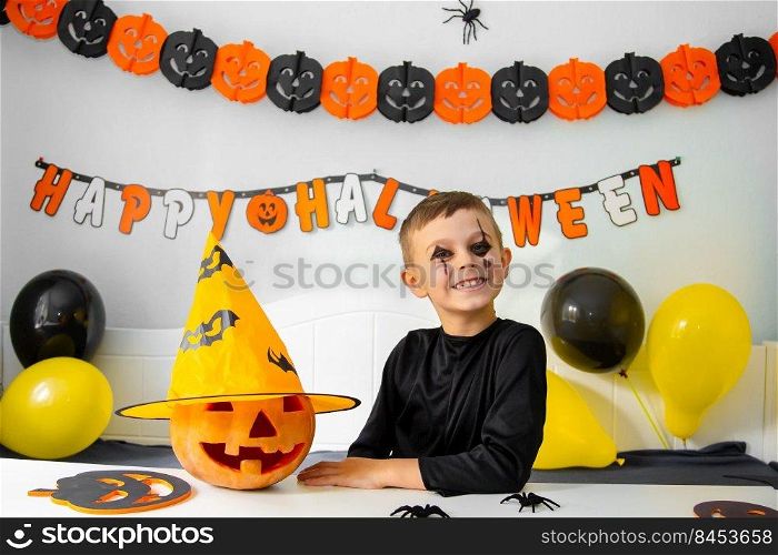 Cute boy in costume sitting behind a table in Halloween theme decorated room. Halloween with safety measures from Covid-19. Halloween holiday concept.. Cute boy in costume sitting behind a table in Halloween theme decorated room. Halloween holiday concept.