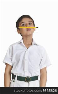 Cute boy in school uniform with pencil between nose and lips over white background