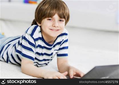 Cute boy lying on floor and using laptop. Playing computer games