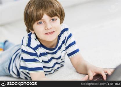 Cute boy lying on floor and using laptop. Playing computer games
