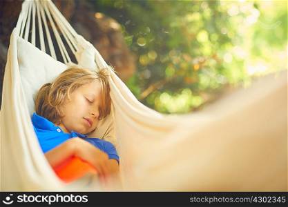 Cute boy reclining in garden hammock asleep