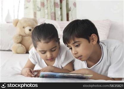 Cute brother and sister reading book in bed