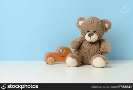 cute brown teddy bear sits on a white table and a wooden children&rsquo;s toy car, blue background