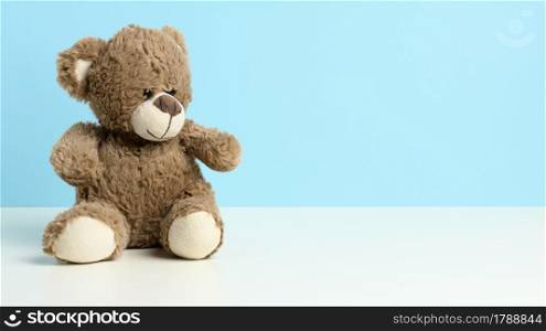 cute brown teddy bear sitting on a white table, blue background, place for an inscription