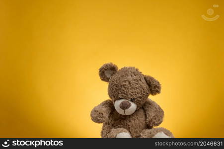 cute brown teddy bear with patches sits on a yellow background, childrens toy
