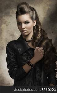 cute brunette female posing in fashion shoot with dark style, casual leather jacket, rock accessories and long wavy hair.