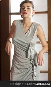 cute brunette female wearing silver elegant dress posing near door with hairdo and stylish make-up