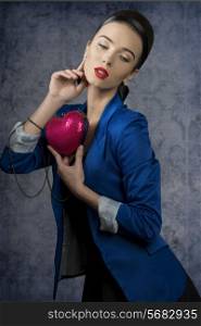cute brunette woman posing with romantic expression and heart shaped bag in the hand, wearing fashion business clothes.