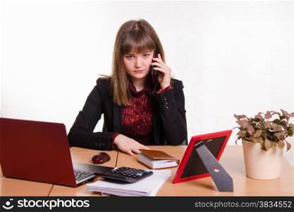 Cute business woman in the office at the computer. The girl behind office table talks on phone