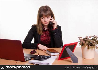 Cute business woman in the office at the computer. girl behind office desk on phone listening to a friend