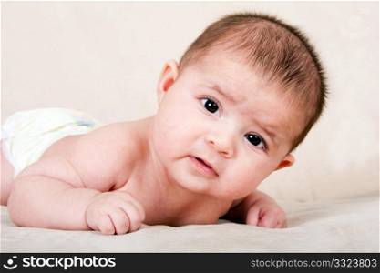 Cute Caucasian Hispanic baby infant laying on belly lifting head making funny expression.
