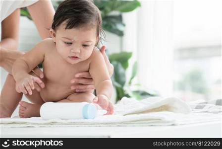 Cute Caucasian little naked toddler baby girl sitting on towel after bathing is playing talcum powder bottle while mother holding and wiping her daughter dry at home. Hygiene care for children concept