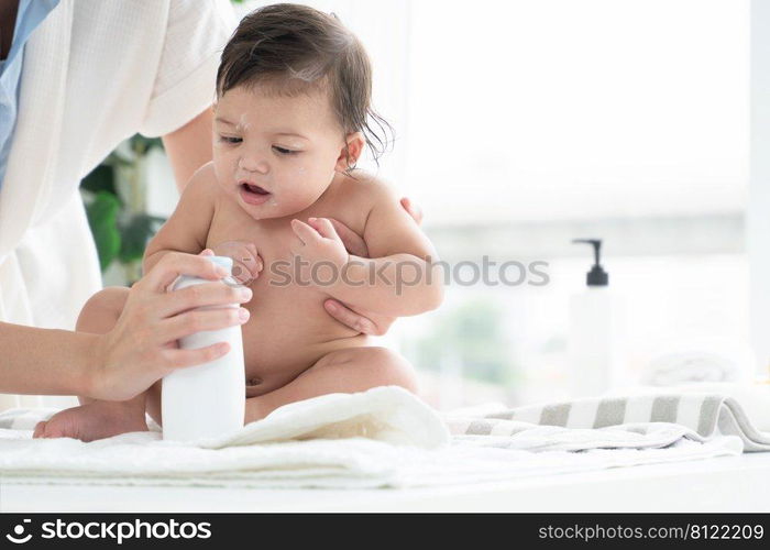 Cute Caucasian little naked toddler baby girl sitting on towel after bathing and wipe body dry while mother open talcum powder bottle and apply on her kid at home. Hygiene care for children concept