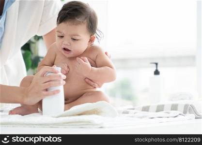 Cute Caucasian little naked toddler baby girl sitting on towel after bathing and wipe body dry while mother open talcum powder bottle and apply on her kid at home. Hygiene care for children concept