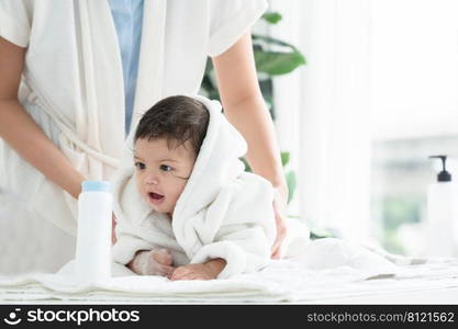 Cute Caucasian little toddler baby girl wear bathrobe after bathing is smiling and lying on towel while mother wipe and apply talcum powder on her body. Hygiene care for children concept